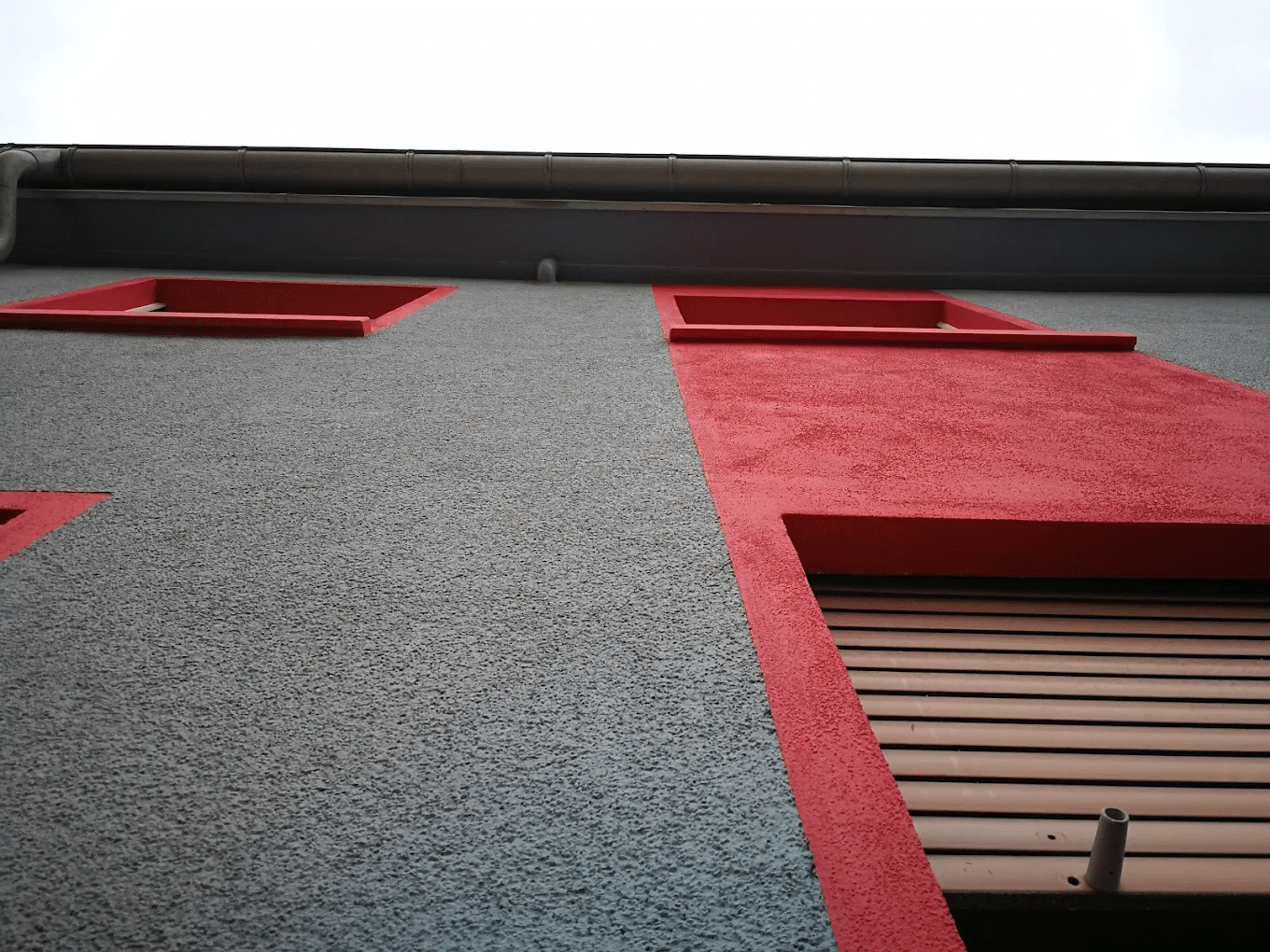Malerbetrieb CasaColor: Blick nach oben an einer frisch gestrichenen Fassade in Grau mit roten Akzenten.